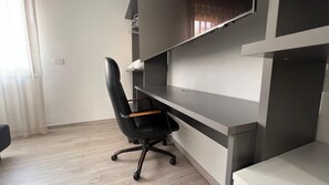 Um espaço de escritório moderno com uma cadeira de escritório preta, uma mesa cinza e uma parede branca.
