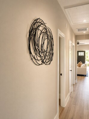 A hallway with a modern abstract wall art piece, white doors, and a wooden floor. - Executive 3BR  Near Downtown, Port & LBJ Hospital (Houston)