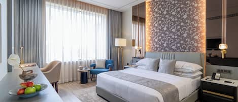 Una habitación de hotel moderna con una cama grande, un escritorio con un florero, una silla y una mesita de noche con una lámpara.