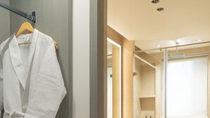 A modern bathroom with a glass shower enclosure, a wooden vanity, and a robe hanging on a rack.