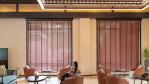 A modern lobby with a seating area, large windows with blinds, and a ceiling with recessed lighting.