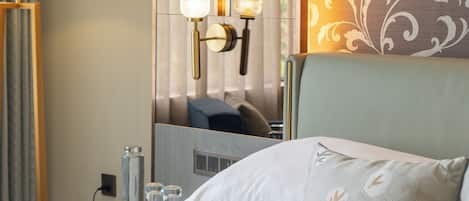 Habitación de hotel con cama, mesita de noche con lámpara, espejo y un papel tapiz con motivos florales.