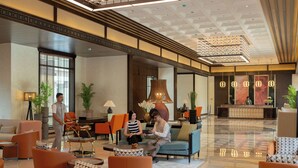 A hotel lobby with seating areas, a reception desk, and a large chandelier.