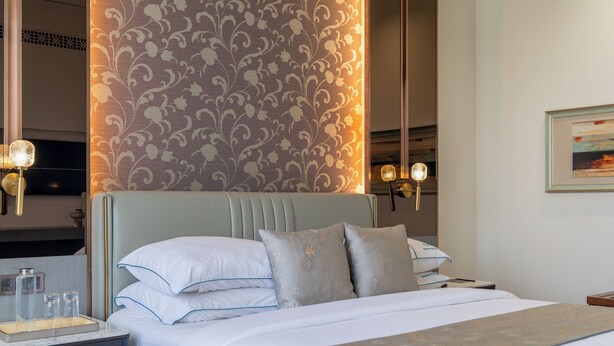 A hotel room with a bed, bedside tables, a nightstand, a mirror, and a wall with a decorative pattern.