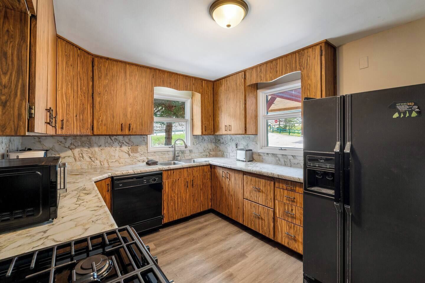 Una cocina con armarios de madera, un refrigerador negro, estufa y lavavajillas.