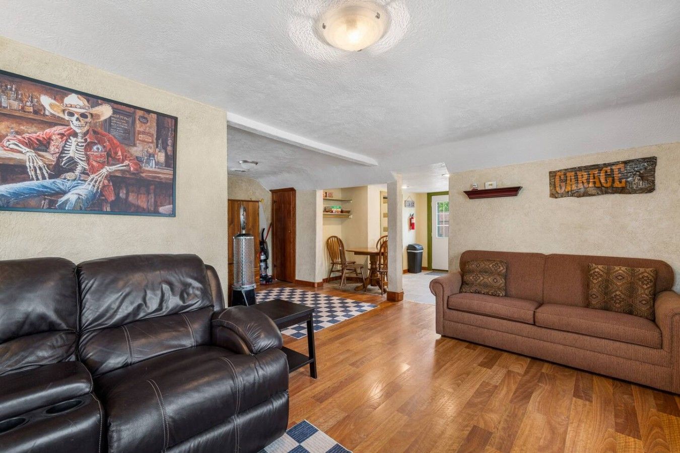 A living room with a leather sofa, a brown couch, and a painting of a skeleton.