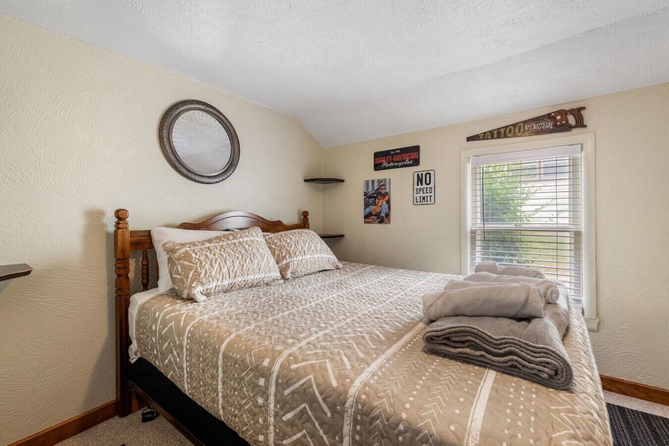 A bedroom with a bed, a round mirror, a 'NO SPEED LIMIT' sign, and a window with blinds.