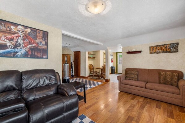 A living room with a leather sofa, a brown couch, and a painting of a skeleton.