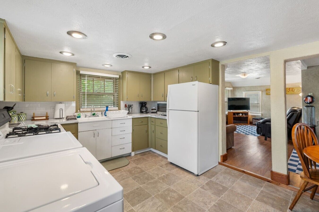 A compact kitchen with a refrigerator, stove, and sink, leading to a dining area with a table and chairs.