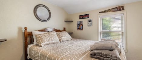 A bedroom with a bed, a round mirror, a 'NO SPEED LIMIT' sign, and a window with blinds.