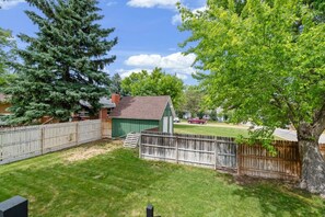 A backyard with a green shed, a wooden fence, and a large tree.