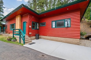 A red log cabin with a green door, a small porch, and a staircase leading to the entrance.