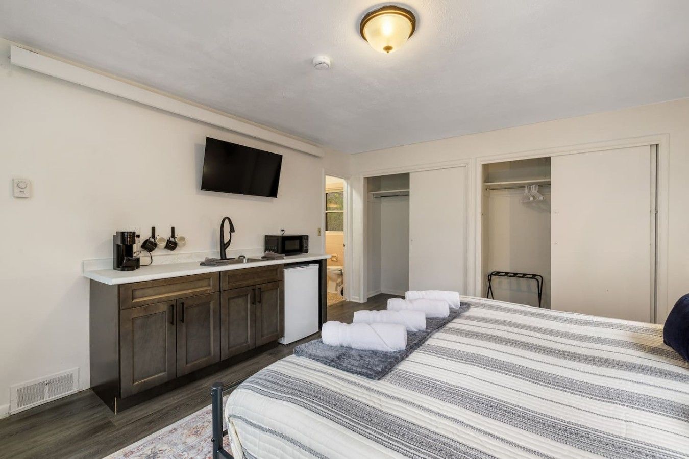 A hotel room with a bed, a small kitchenette, a TV, and a closet.