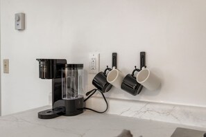 Un taulell de cuina amb una cafetera, un dispensador d'aigua i dues tasses penjades a la paret.