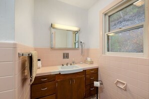 A bathroom with a double sink, wooden cabinets, a towel rack, a window, and a mirror.