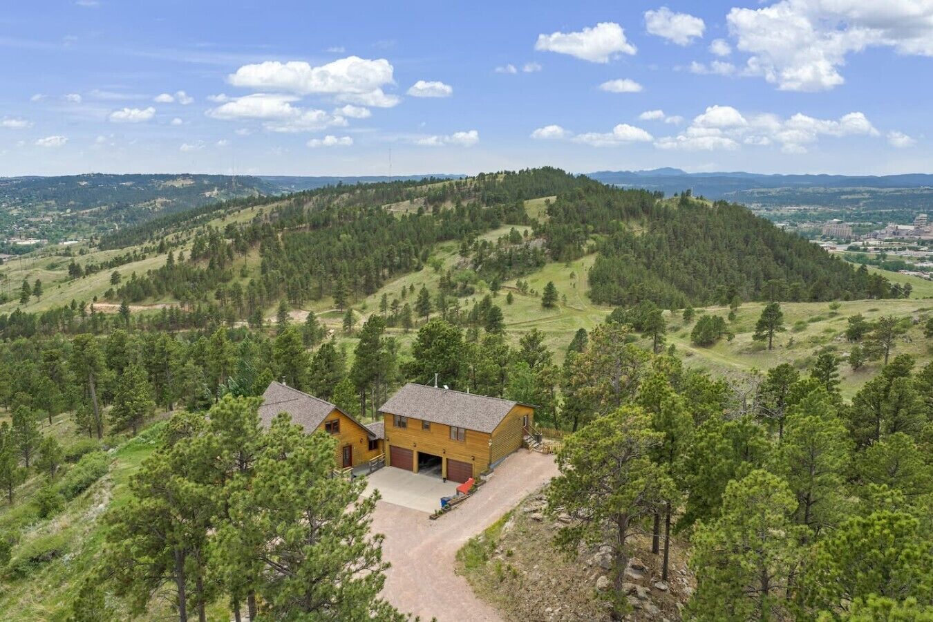 A two-story log cabin with a garage, surrounded by a forested hillside.