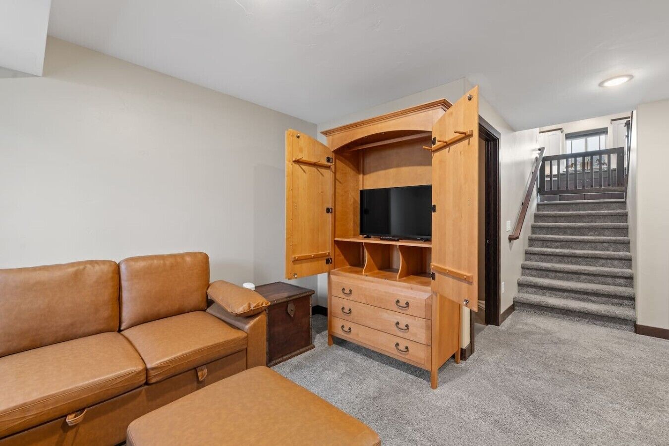A compact living space with a sofa, a wooden entertainment unit with a TV, and a staircase.