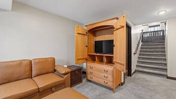 A compact living space with a sofa, a wooden entertainment unit with a TV, and a staircase.