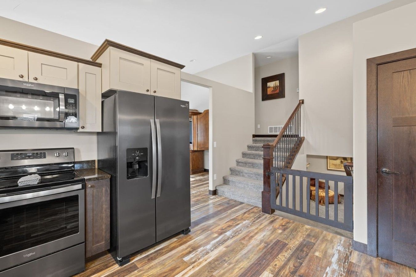 A modern kitchen with stainless steel appliances, a wooden staircase, and a view to the living area.