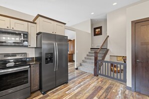 A modern kitchen with stainless steel appliances, a wooden staircase, and a view to the living area. - 3BR 2BA, Spearfish Retreat, Deck & Fenced Yard (Spearfish)