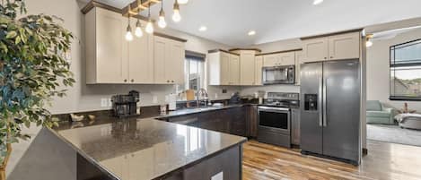 A modern kitchen with a central island, stainless steel appliances, and a hanging light fixture.