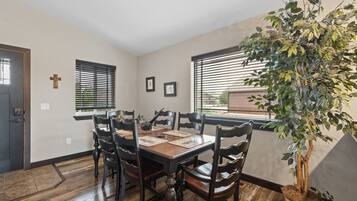 A dining room with a wooden table and chairs, a cross on the wall, and a large plant.