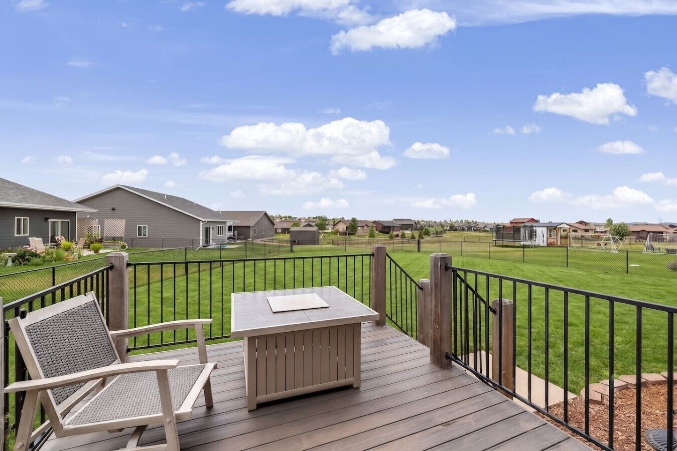 A deck with a table and chairs, overlooking a well-maintained lawn and neighboring houses.