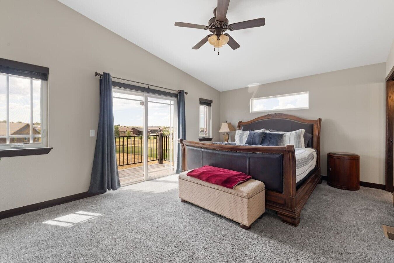 A bedroom with a bed, a bench, a ceiling fan, and a view through a sliding glass door.