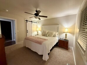 Ein Schlafzimmer mit einem Bett, Deckenventilator, Nachttischlampen, einem Nachttisch und einer Tür.