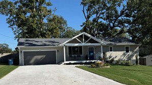 A single-story house with a garage, a front porch, and a well-maintained lawn. - Two Tired Inn: Cozy, convenient, hot tub, fire pit, by trails, museums, downtown (Bentonville)