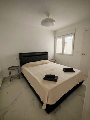 Ein Schlafzimmer mit einem Bett, einem kleinen Tisch, einem Fenster und einer Tür.