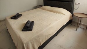 Uma cama com cabeceira escura, um cobertor bege e duas toalhas enroladas.