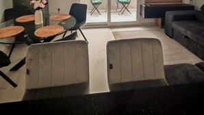 Uma sala de estar com mesa de vidro, cadeiras, sofá, televisão e varanda com cadeiras.