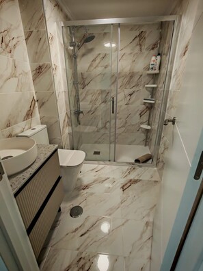 Ein Badezimmer mit einer gläsernen Duschkabine, einer Toilette und einem Waschbecken mit Marmorplatte.