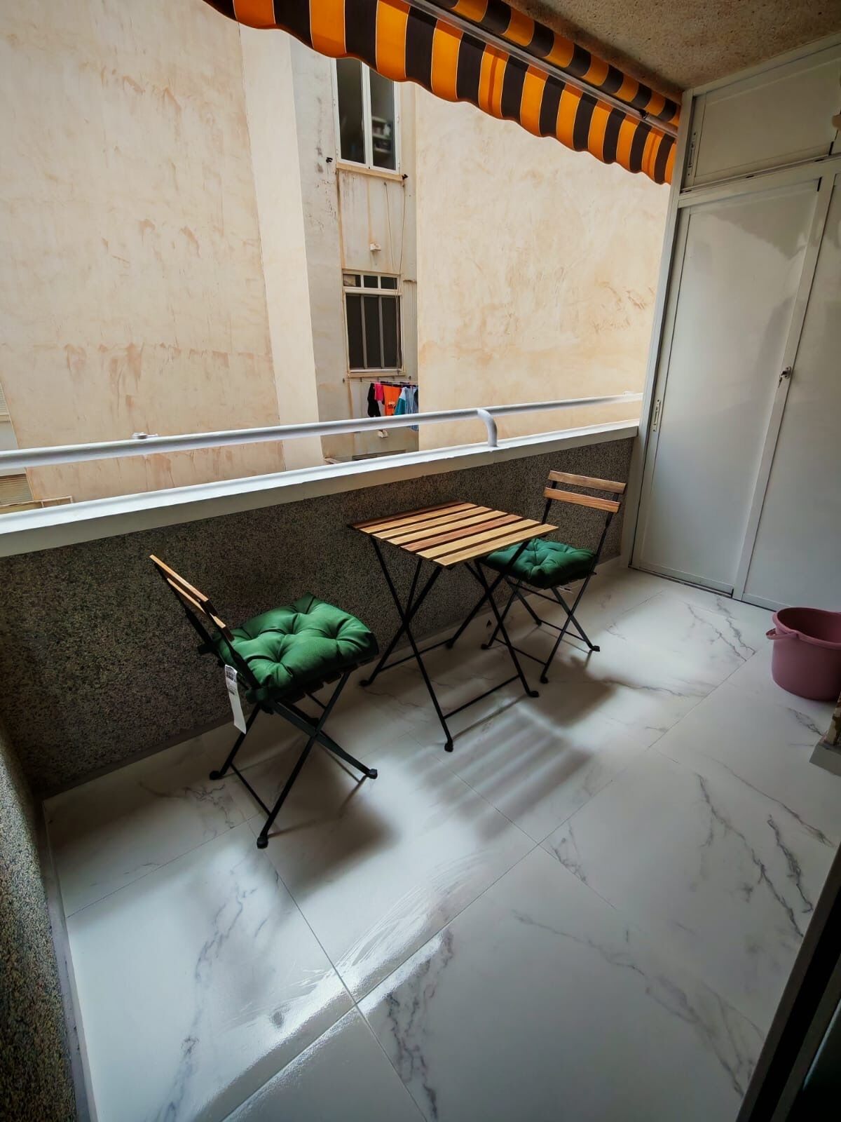 A balcony with a metal railing, a small table, and two green cushioned chairs.