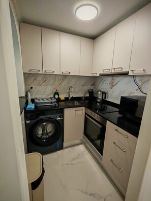 A compact kitchen with a washing machine, oven, and a coffee maker. - La Casa Datskovi Beach Apartments (Torre Vieja)