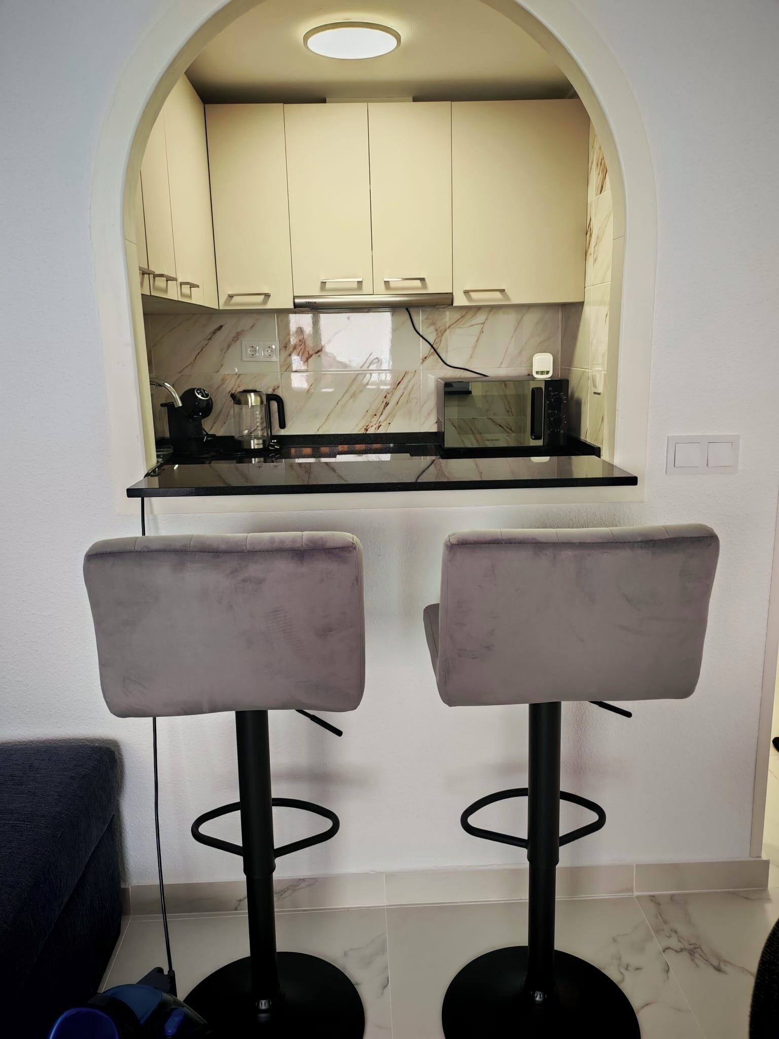 A kitchen with a marble countertop, two bar stools, and a recessed ceiling light.