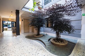 A spacious indoor area with a terrazzo floor, two potted trees, and a view of the outside through a glass wall. - HOTEL BOUTIQUE POMA ROSA (Medellin)