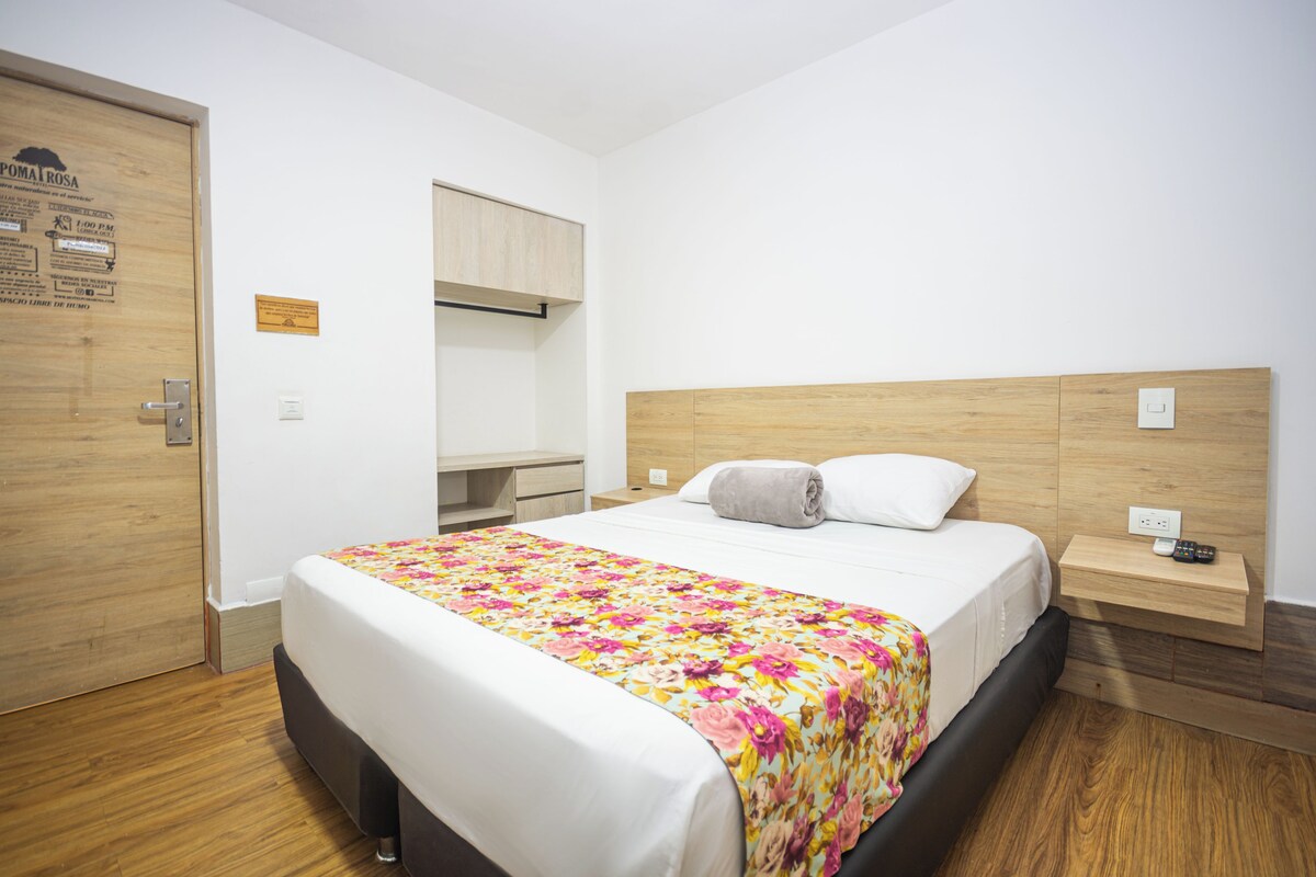 A hotel room with a bed, a wooden headboard, a bedside table with a remote control, and a door with a wooden panel.