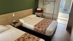 Une chambre d’hôtel avec deux lits, un bureau, une chaise, un porte-manteau et une vue sur l’extérieur.