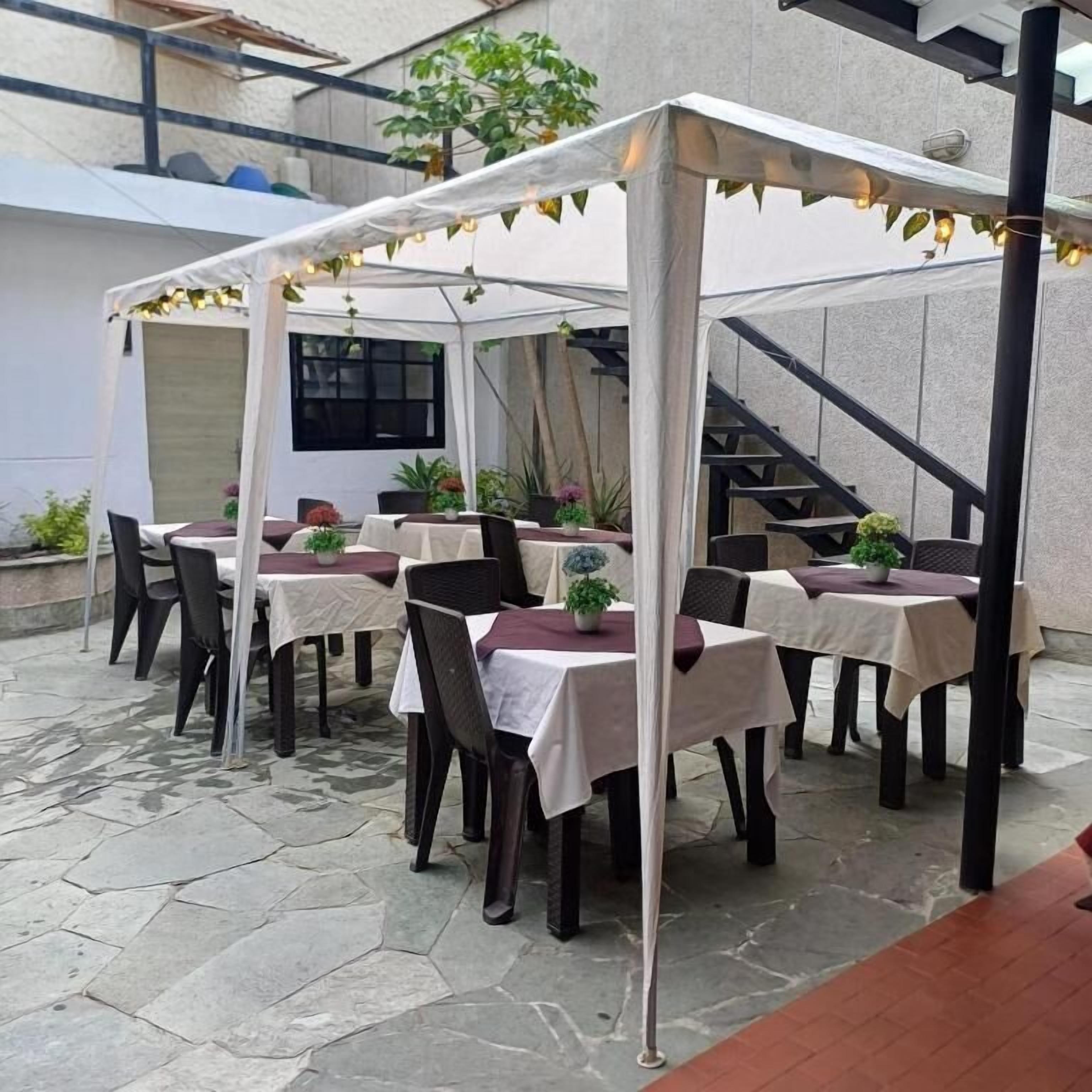Een terras buiten met tafels en stoelen, een overdekt zitgedeelte en een trap op de achtergrond.