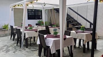 Een terras buiten met tafels en stoelen, een overdekt zitgedeelte en een trap op de achtergrond.
