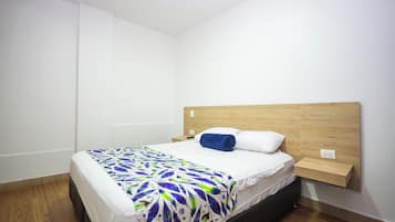 Ein Einzelbett mit einem gemusterten Überwurf, ein hölzernes Kopfteil, ein Nachttisch und eine Steckdose an der Wand.
