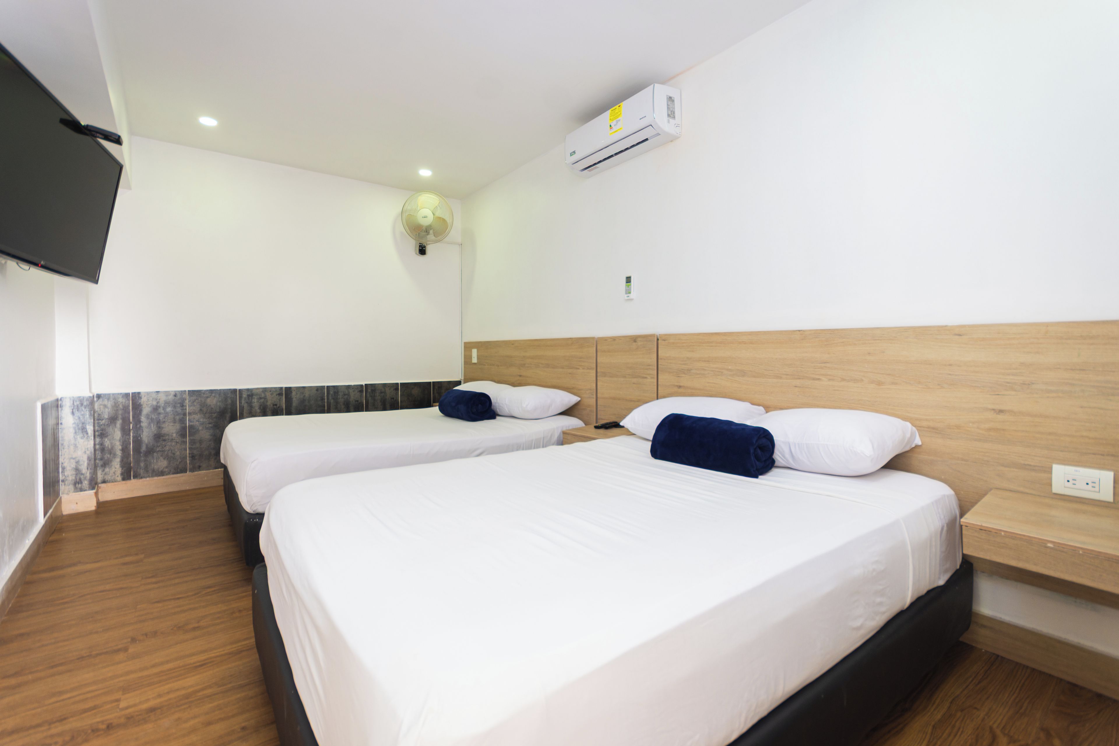 A hotel room with two beds, a flat-screen TV mounted on the wall, and an air conditioning unit above the beds.