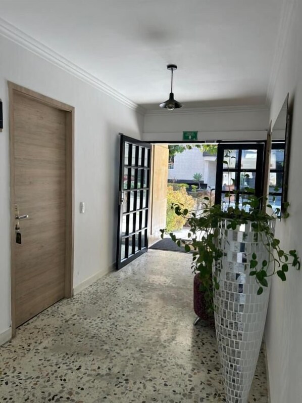 A hallway with a wooden door, a tiled floor, a potted plant, and a view through a glass door. - HOTEL BOUTIQUE POMA ROSA (Medellin)