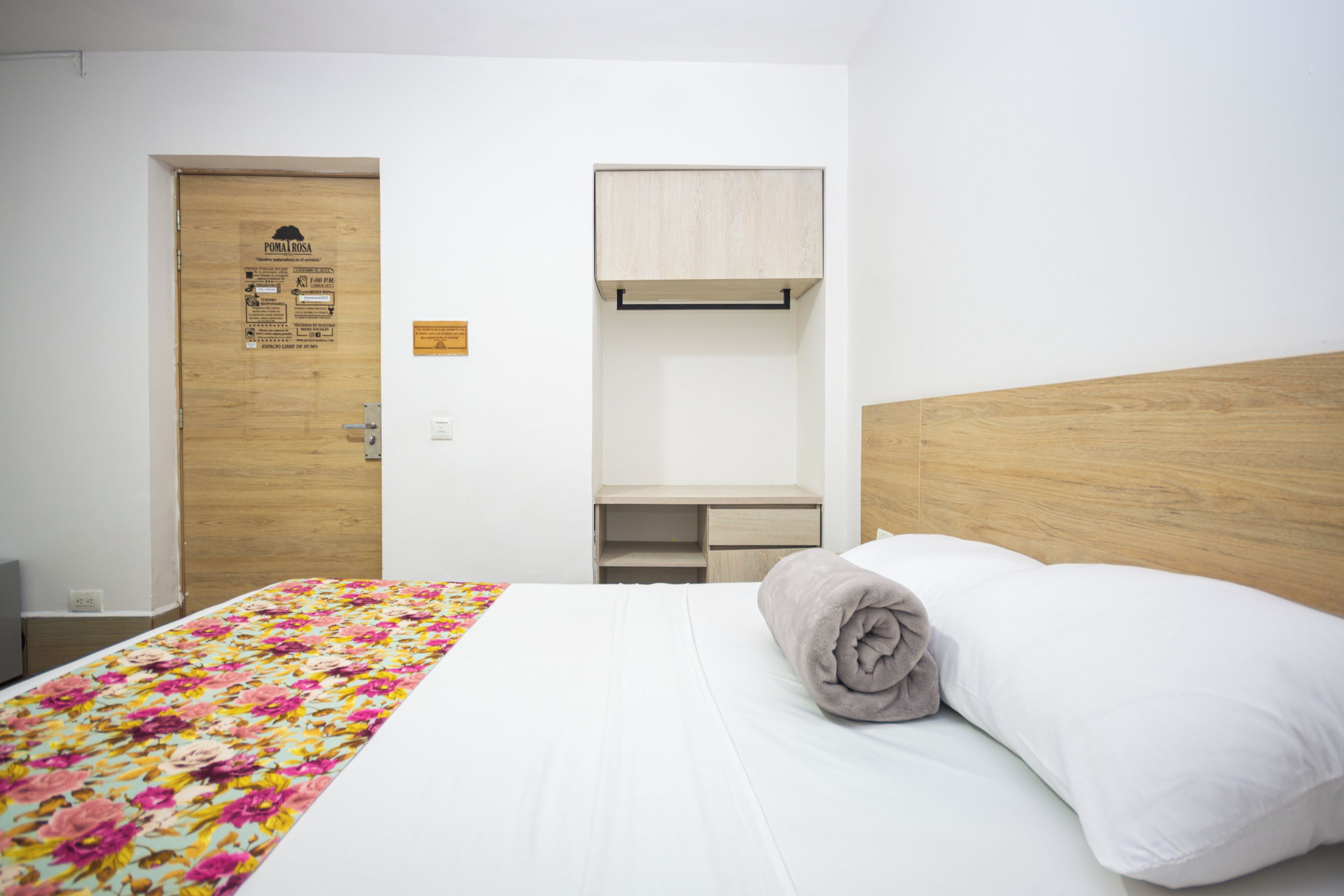 Una habitación de hotel con una cama, cabecera de madera, escritorio y una puerta con un letrero.