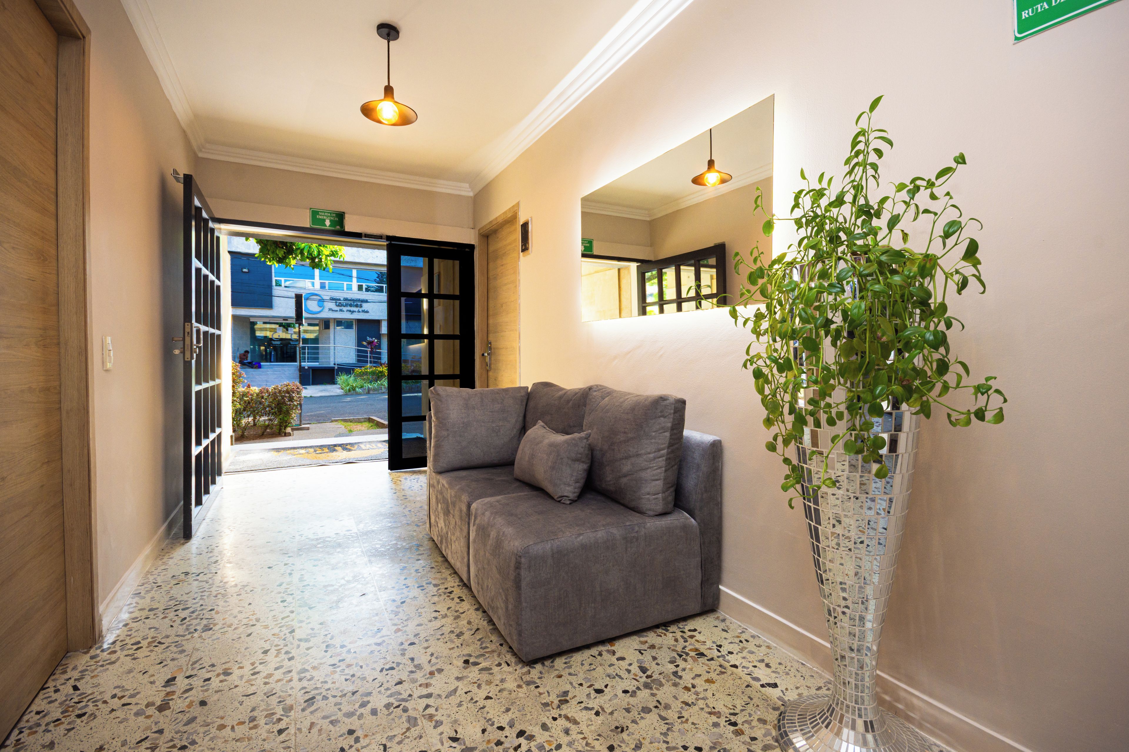 Eine Hotelhalle mit einem grauen Sofa, einer hohen Pflanze im Topf und einem Terrazzo-Boden.