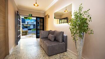 Een hotellobby met een grijze bank, een hoge potplant en een terrazzovloer.