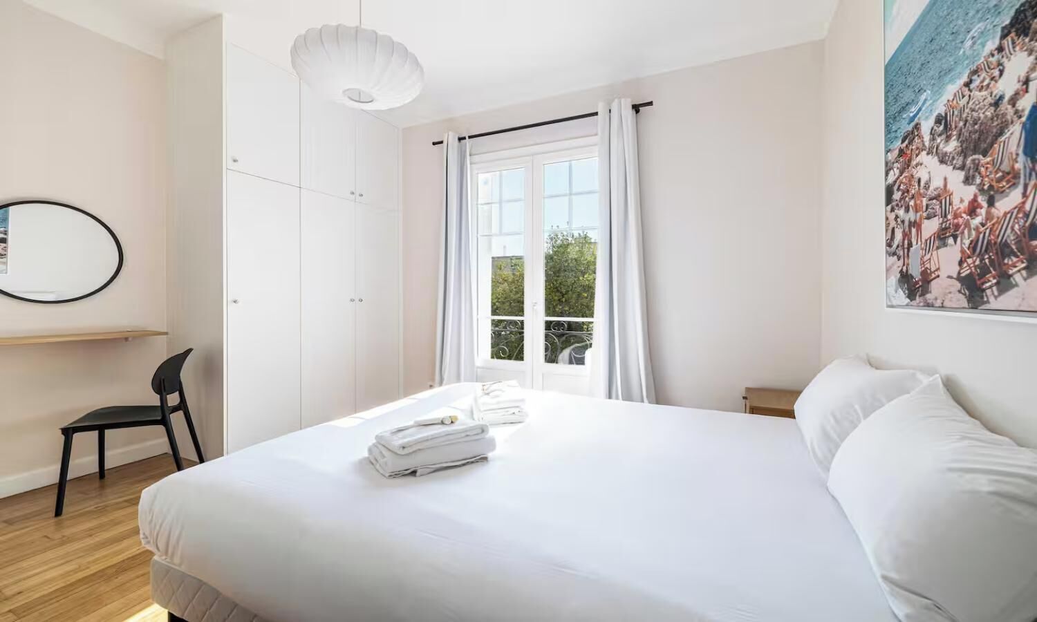 A hotel room with a large bed, a desk with a chair, a window with curtains, and a painting on the wall.