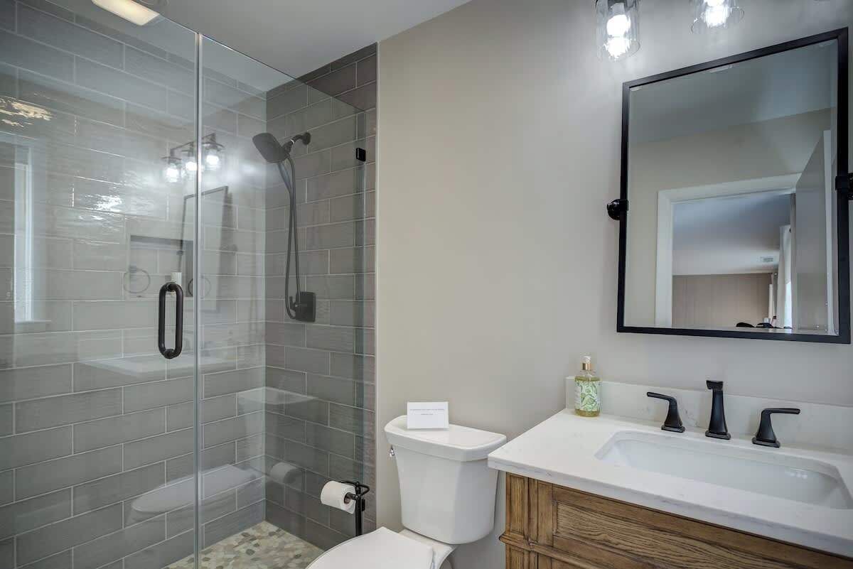 Un baño moderno con ducha de vidrio, inodoro blanco y tocador con espejo.